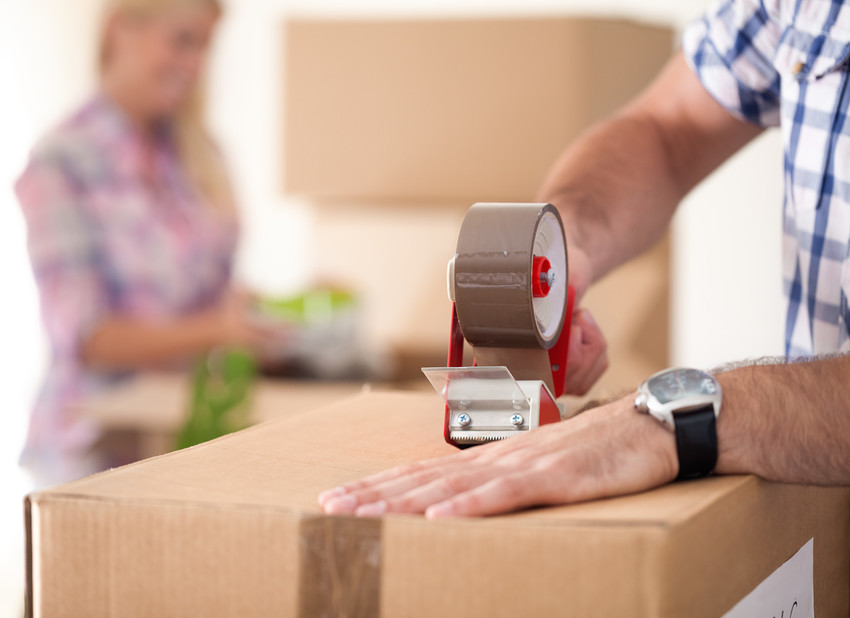 two people taping up cardboard moving boxes