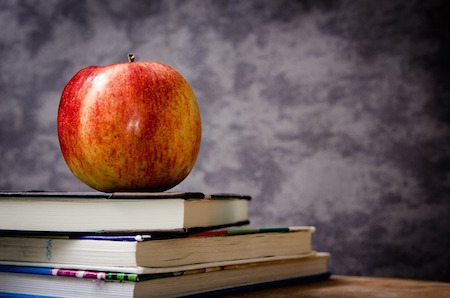 An apple sitting on top of three school textbooks.