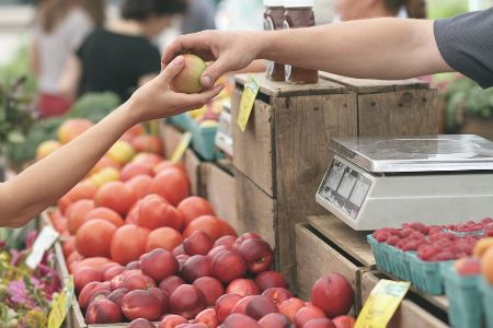 A vendor handing someone an apple from a produce stand.