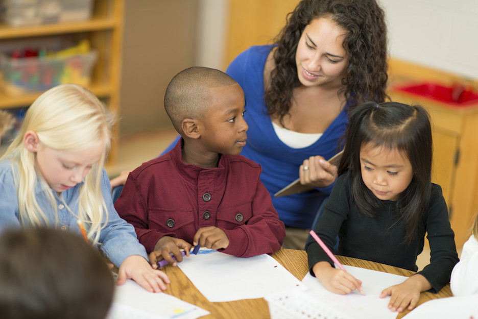 Teacher sitting with young students at a round table.