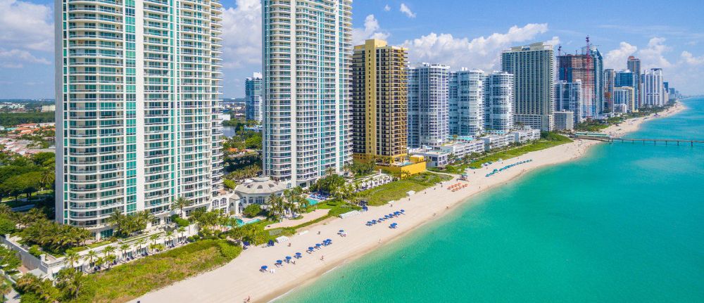 Aerial view of the white sands of Sunny Isles Beach with high-rise condos in the foreground.