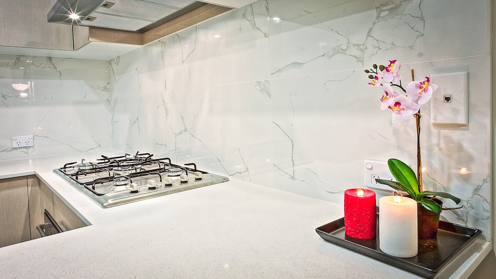 A modern and sparsely decorated kitchen with granite countertops, marble backsplash, and white cabinets.