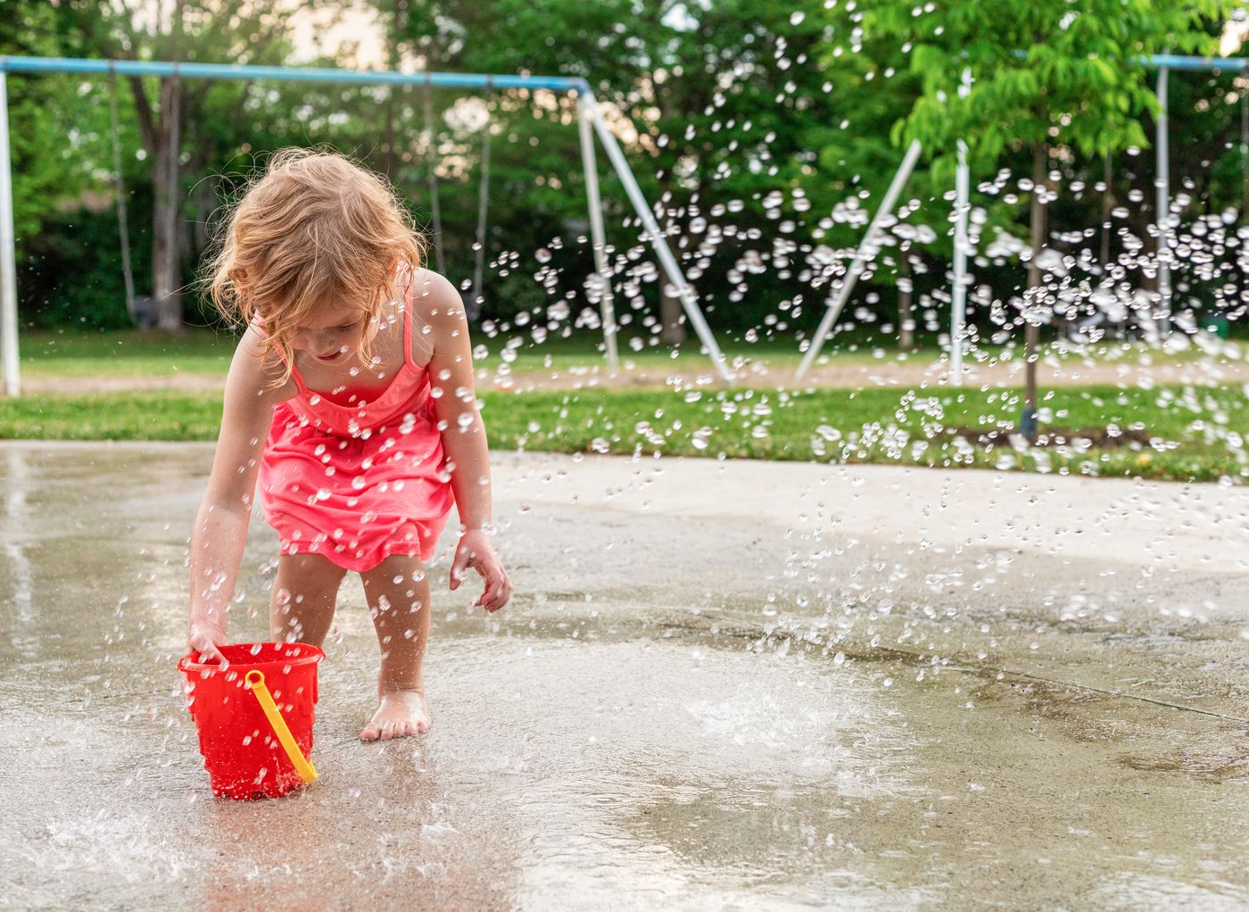 Toddler playing with a bucket at a park splash pad