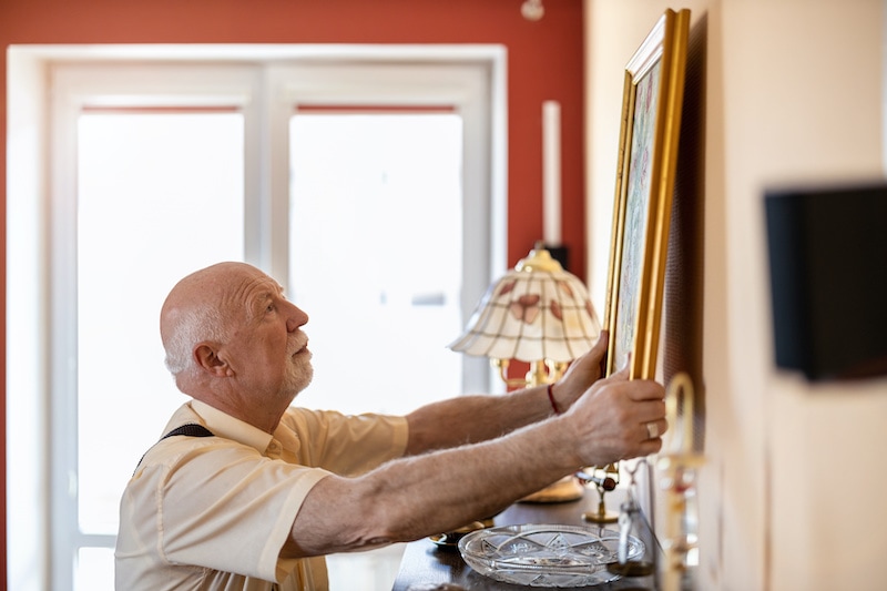 An elderly man removing photo frame from wall